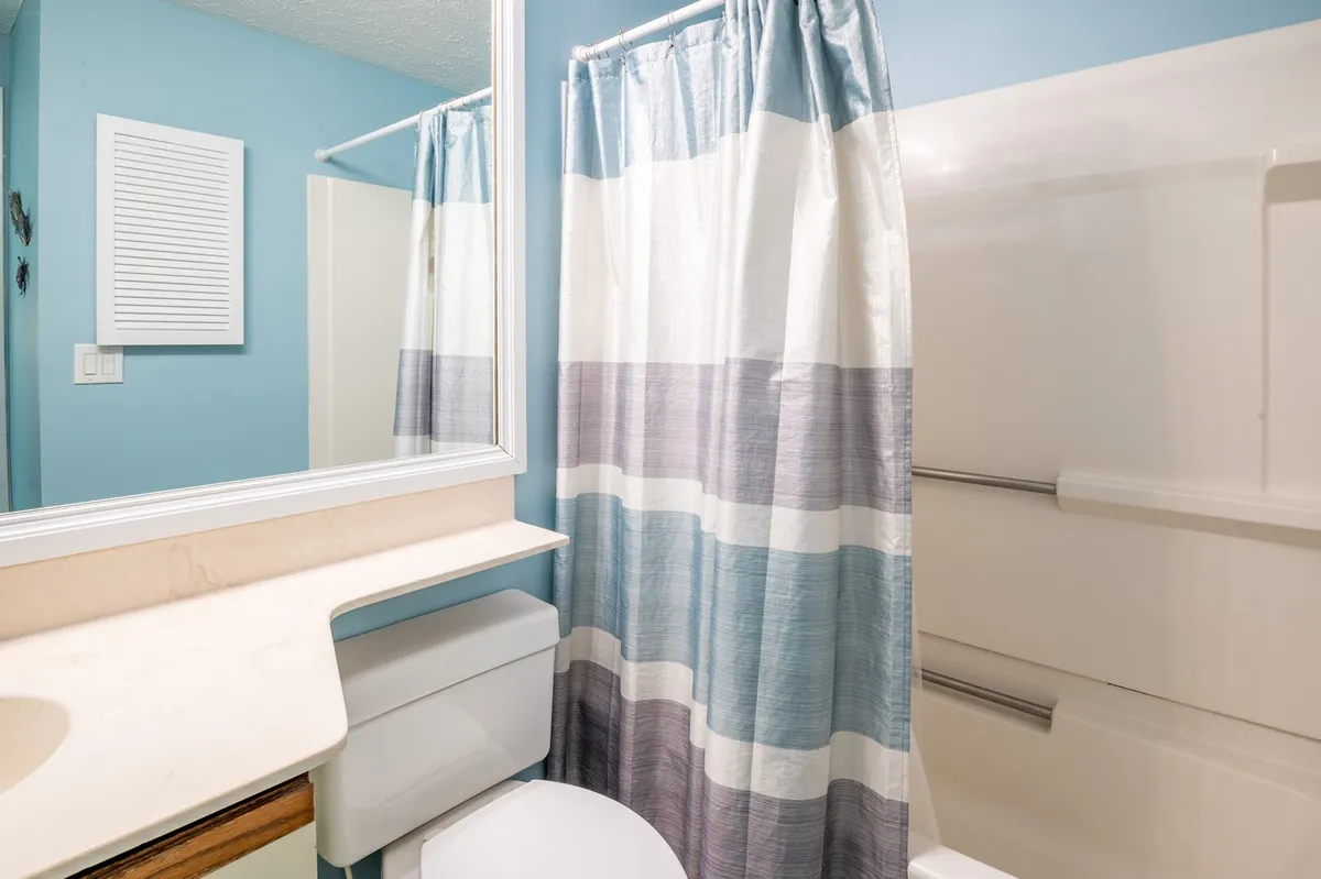 A fresh, well-lit bathroom with a large mirror, elegant sink, and a shower curtain in calming hues. The space is functional yet inviting, offering a refreshing setting for morning routines or evening relaxation.