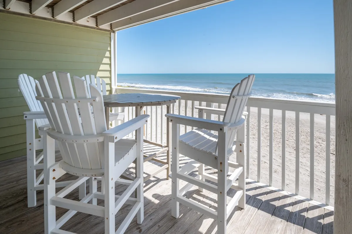 A private balcony with high white chairs and a wooden table overlooking the shimmering Atlantic Ocean. The serene setting is ideal for relaxing, enjoying drinks, or simply marveling at the view as the sun rises or sets.