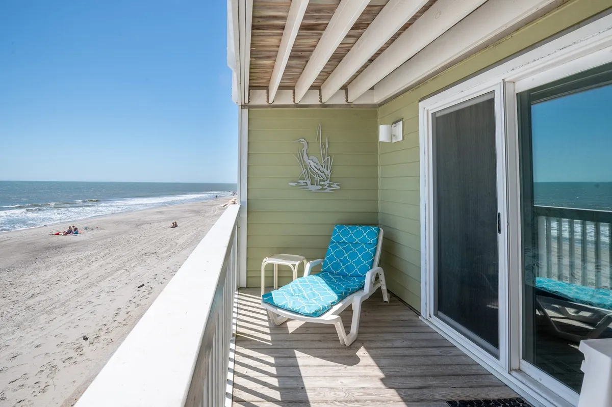 A tranquil beachfront vista with a lounge chair and table set just above the sand, facing out to a broad expanse of ocean. The scene is peaceful and inviting, ideal for morning sunrises, sunbathing, or simply soaking in the coastal atmosphere.