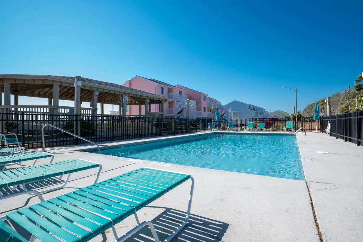This image shows an outdoor swimming pool surrounded by lounge chairs, with colorful buildings in the background. The setting is open and relaxed, evoking a resort-like atmosphere for guests to enjoy swimming, sunbathing, or social gatherings beside the water.