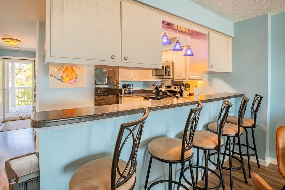 A bar counter with comfortable stools, adjacent to a well-equipped kitchen and illuminated by elegant light fixtures. The setup encourages socializing over breakfast or drinks, directly linking the kitchen and living areas.