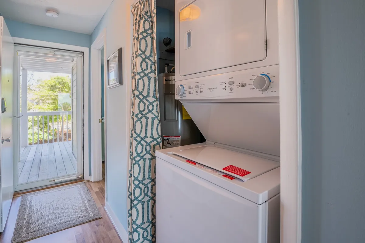 A compact laundry area featuring a stacked washer and dryer, accentuated by natural light from an adjacent open doorway. A decorative curtain adds a homely touch, while the practical layout ensures easy access to laundry facilities.