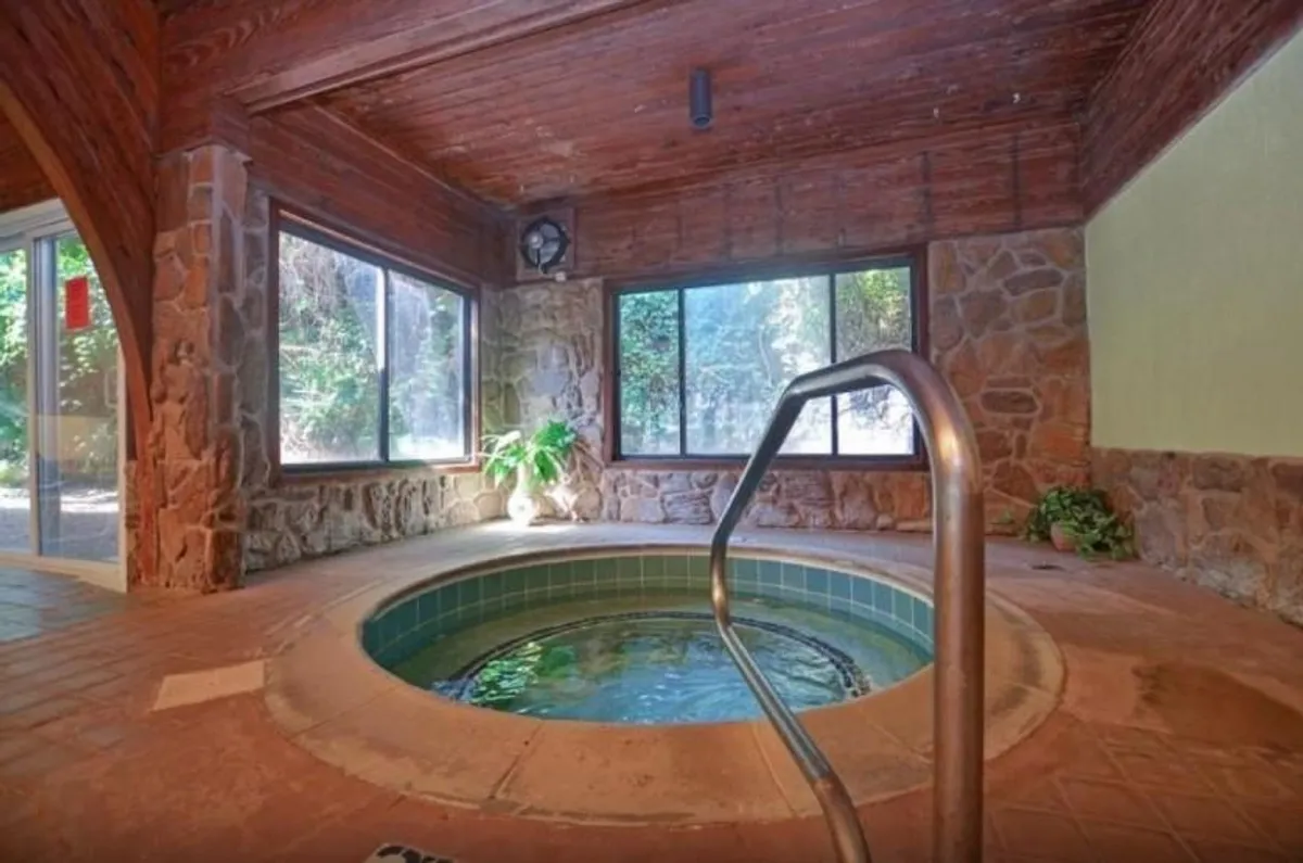 A serene indoor hot tub area with natural stone walls, wooden ceilings, and expansive windows that allow for beautiful views outside. The space exudes calm and luxury, offering a perfect spot for relaxation and socializing after a day of activities.
